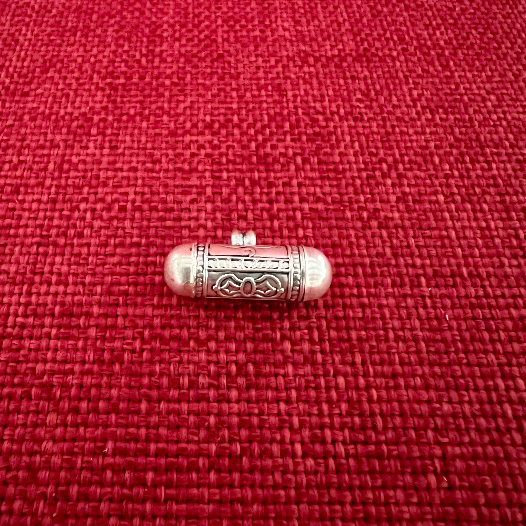 2.3cm long silver horizontal cylinder locket embossed with Tibetan Om, Buddha Eyes and the dorje symbol and contains scroll with Om Mani Padme Hung mantras inside