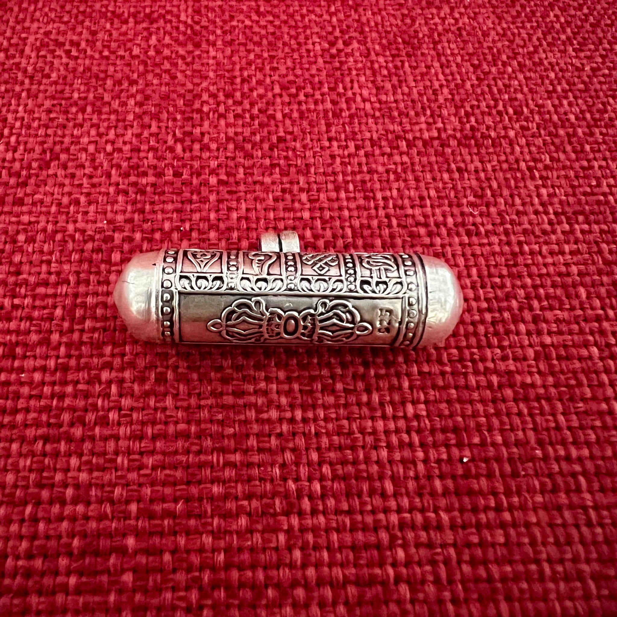 4cm long silver horizontal cylinder locket embossed with 8 auspicious symbols and dorje and scroll with Om Mani Padme Hung mantras inside