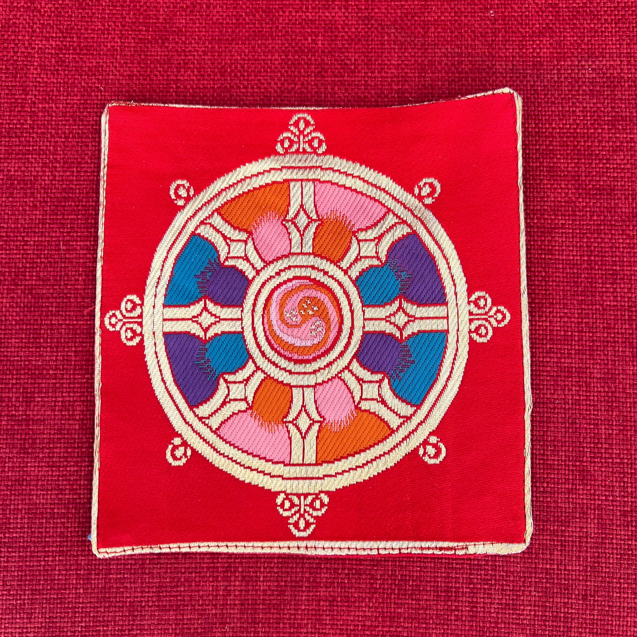 Red brocade Bell and Dorje mat with dharma wheel symbol in centre