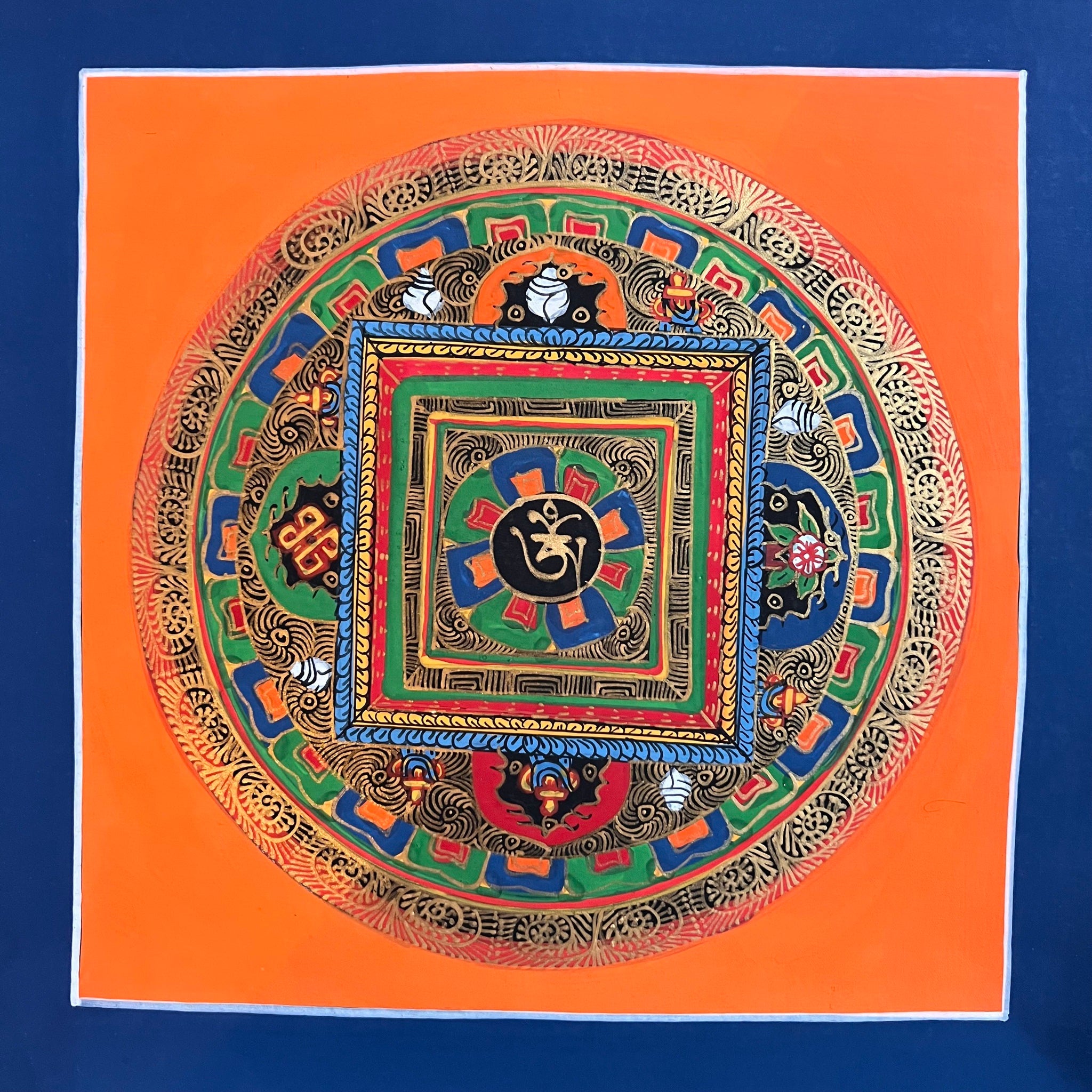 26.5cm Square Mandala Painting with the Tibetan Om symbol inside a lotus shape with surrounding Tibetan Auspicious Symbols and an orange background with blue border