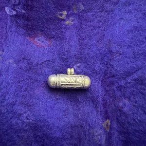 2.3cm long silver horizontal cylinder locket embossed with Tibetan Om, Buddha Eyes and the dorje symbol and contains scroll with Om Mani Padme Hung mantras inside