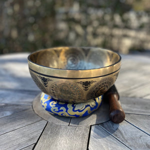 Bronze coloured 21cm singing bowl with black carving of Ganesh, Hindu OM symbol, and mandala designs, pictured with wooden striker and blue donut cushion